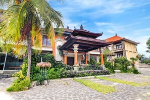 A traditional building with a tiled roof, a covered entrance, and a garden with palm trees and plants. - Spacious Family Suite With Free Wifi and Parking (Denpasar)