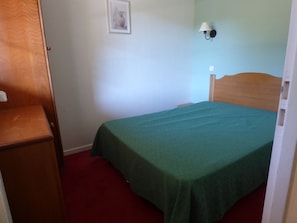 Ein Zimmer mit einem Bett, einem Nachttisch, einer Wandlampe und einem gerahmten Bild.
