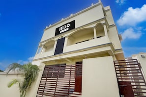 A hotel building with a sign indicating it's a company-serviced hotel, a gated entrance, and a palm tree in the foreground.