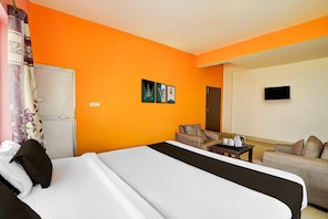 A hotel room with an orange wall, a bed with white and black bedding, a small table with a kettle, and a sofa.