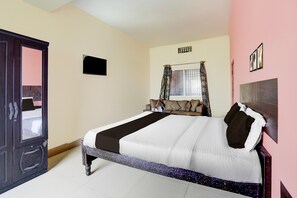 A bedroom with a bed, a wardrobe, a window with curtains, and a wall-mounted TV.