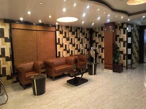 A lobby with a brown leather sofa, a trash bin, a floor lamp, and a patterned wall.