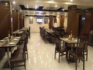A restaurant with multiple dining tables and chairs, a polished marble floor, and a person standing in the background.