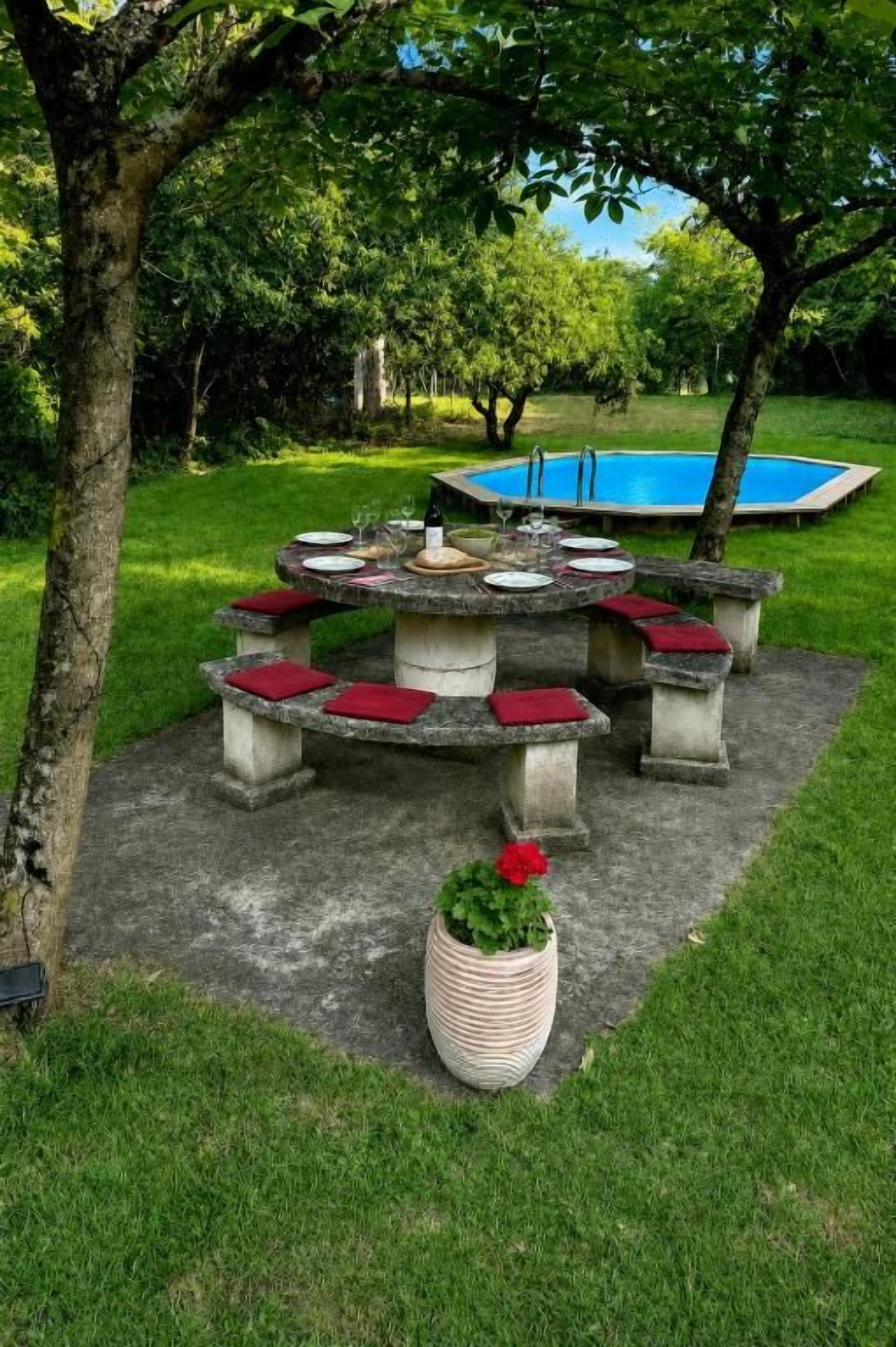 Área de estar ao ar livre com assentos circulares, almofadas vermelhas, uma mesa de concreto e um vaso de planta.