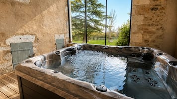 Un bain à remous avec une terrasse en bois, un mur en pierre et une vue sur les arbres par une fenêtre.