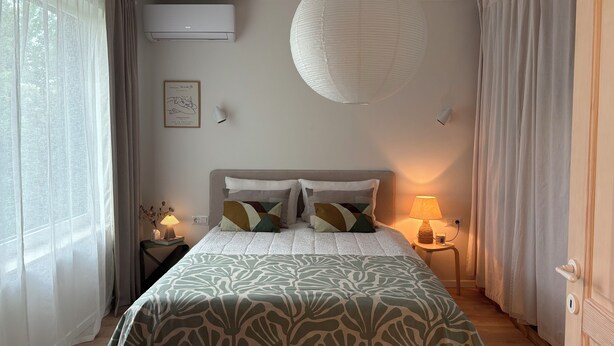 A bedroom with a bed, bedside lamps, a wall-mounted air conditioner, and a hanging light fixture. - Central Park View Apartment with a terrace and lake views features (Dobrich)