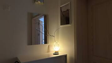 Une pièce avec un miroir, un tableau encadré et une lampe allumée posée sur une commode.