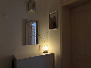 A room with a mirror, a framed picture, and a lit lamp on a cabinet.