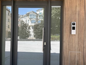 A door with a keypad lock and a view of a building with multiple windows and balconies.
