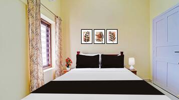A hotel room with a bed, a nightstand, a lamp, a window with curtains, and three framed pictures on the wall.