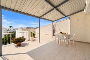 A covered outdoor patio with a table and chairs, potted plants, and a view of the cityscape. - 2BR Apartment with Pool - Aphrodite by Premier (Ayia Napa)