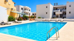 A swimming pool with sun loungers and a covered area, surrounded by modern buildings. - 2BR Apartment with Pool - Aphrodite by Premier (Ayia Napa)