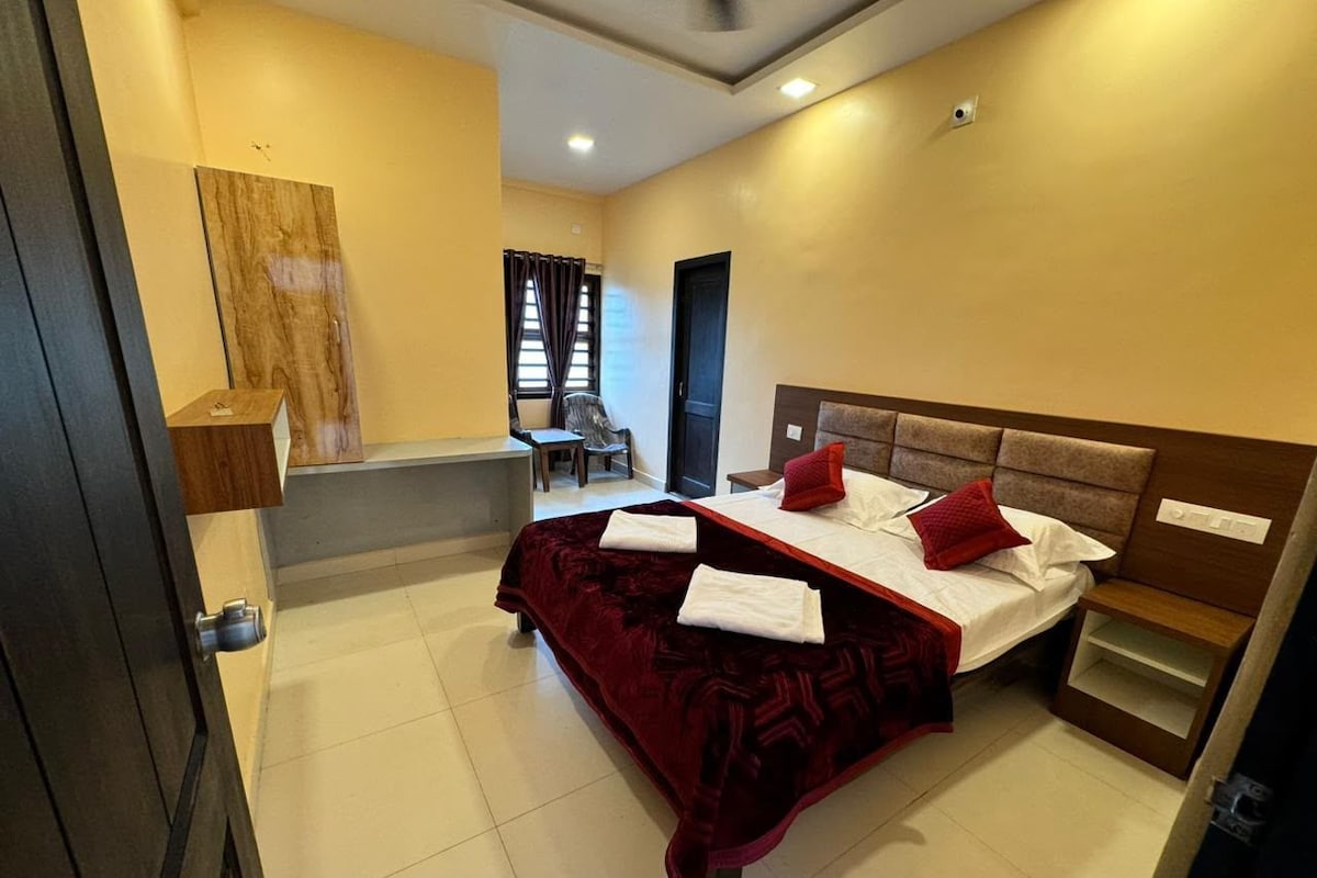 A hotel room with a bed, a small desk, a chair, and a window with curtains.