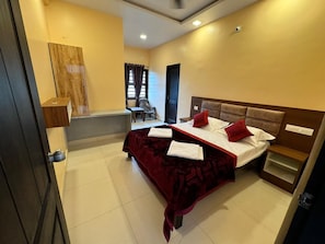 A hotel room with a bed, a small desk, a chair, and a window with curtains. - KVK Beach Residency (Murdeshwar)