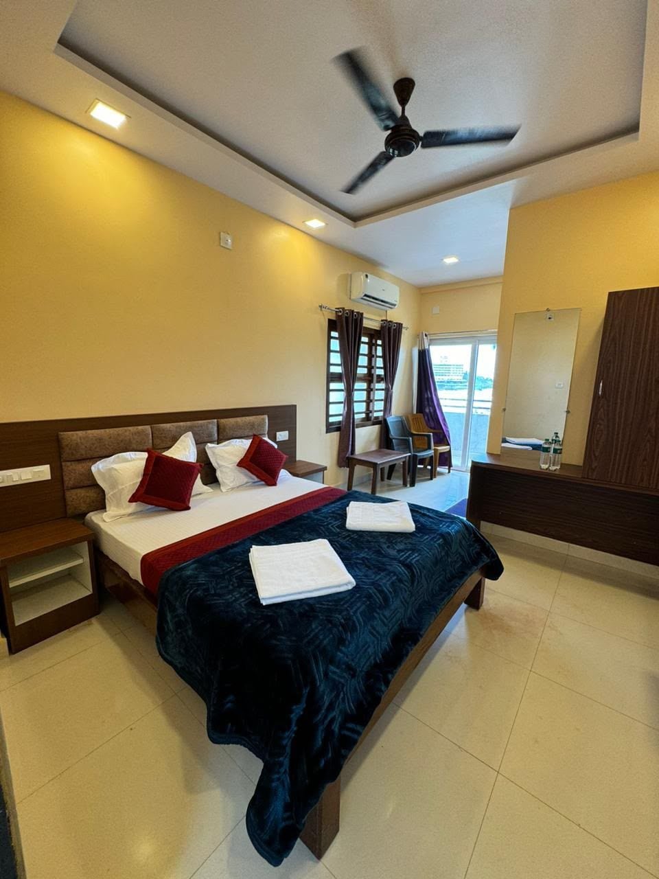 Habitación de hotel con cama, mesitas de noche, ventilador de techo y ventana con cortinas.