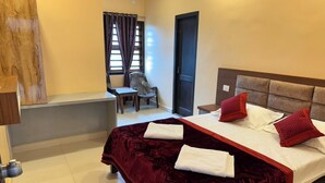 A hotel room with a large bed, two pillows, a chair, a desk, and a window with curtains. - KVK Beach Residency (Murdeshwar)