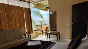 A hotel room with a bed, a sofa, a small table, and a view of the outdoors. - KVK Beach Residency (Murdeshwar)