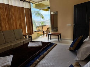 A hotel room with a bed, a sofa, a small table, and a view of the outdoors. - KVK Beach Residency (Murdeshwar)