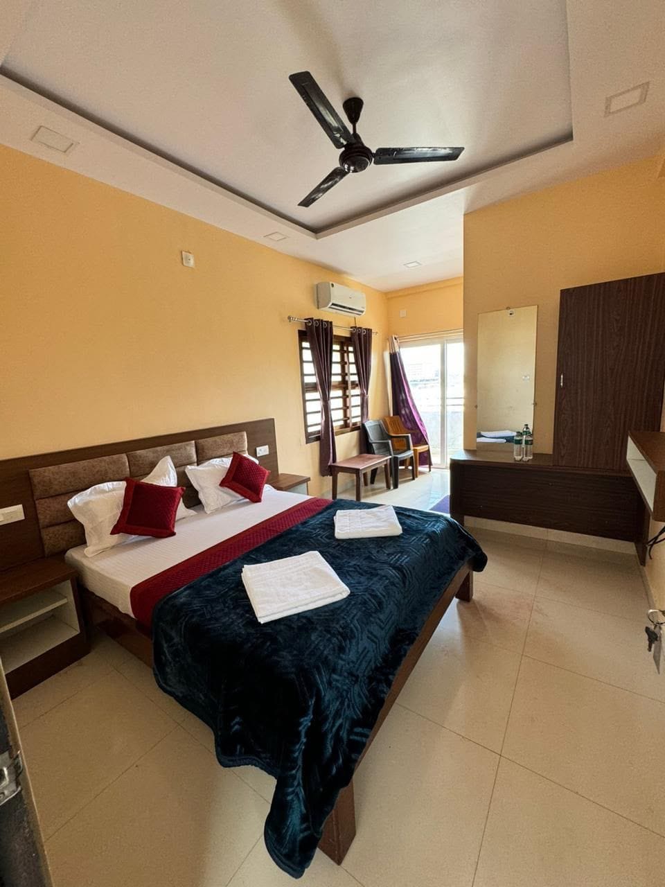 A hotel room with a bed, a desk, a chair, a wardrobe, and a ceiling fan.
