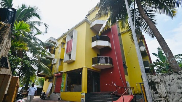 A multi-story building with a yellow facade, red accents, and a staircase leading to the entrance. - KVK Beach Residency (Murdeshwar)