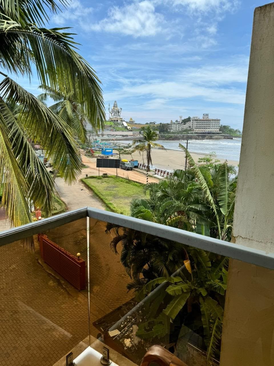 Een balkon met uitzicht op een strand, palmbomen en een groot gebouw in de verte.