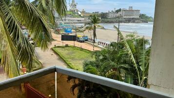 Een balkon met uitzicht op een strand, palmbomen en een groot gebouw in de verte.