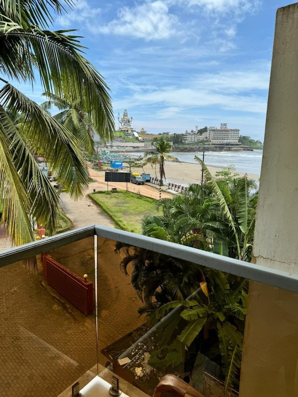 A balcony with a view of a beach, palm trees, and a large building in the distance.