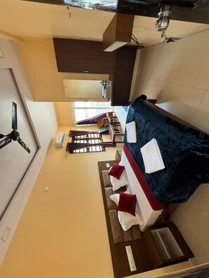 Habitación de hotel compacta con cama, un pequeño escritorio, una silla, una ventana y un ventilador de techo.