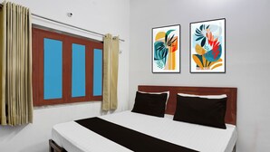 Habitación de hotel con cama, dos almohadas, ventana con cortinas y dos cuadros abstractos en la pared.