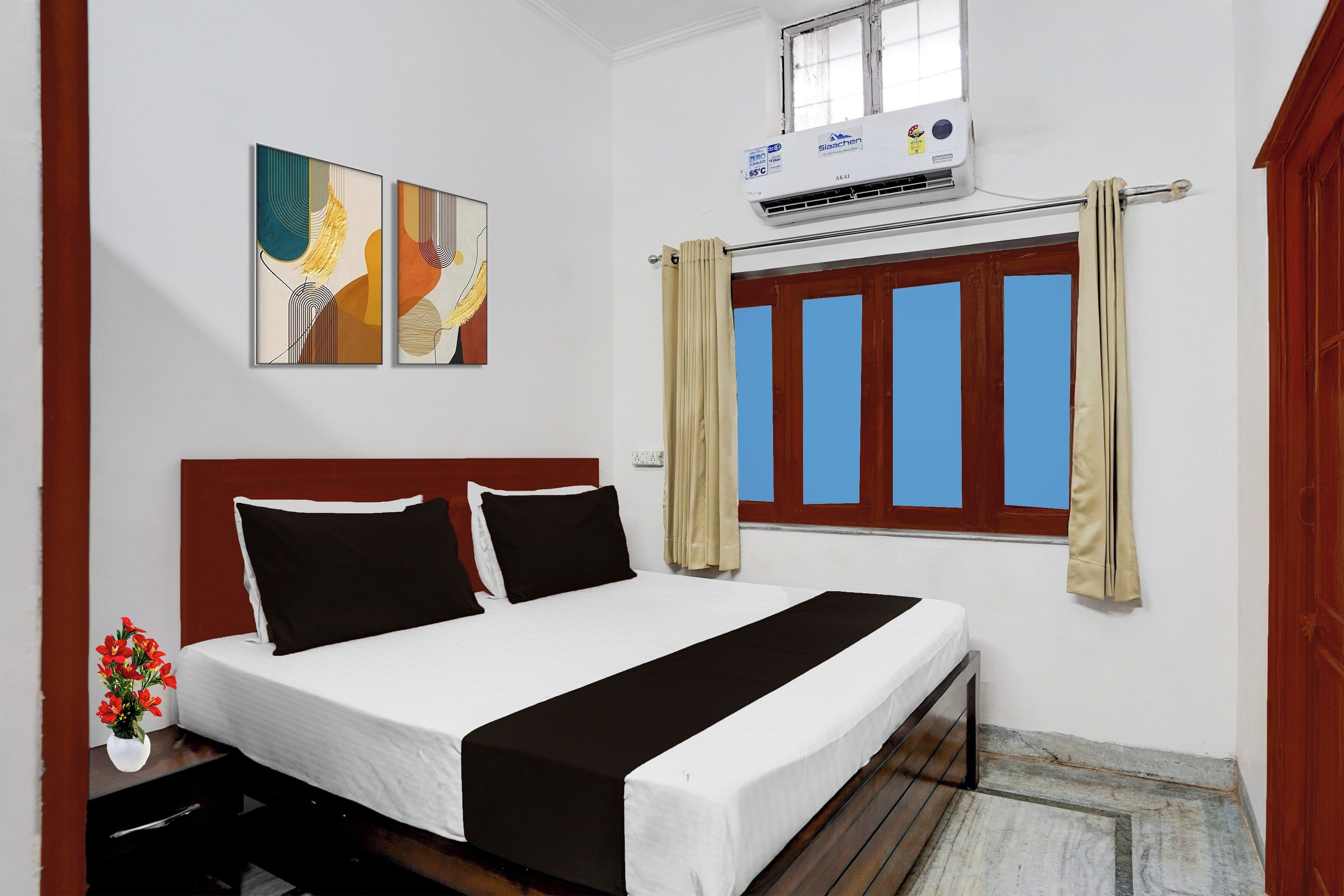 A hotel room with a bed, a window with curtains, an air conditioning unit, and two wall-mounted artworks.
