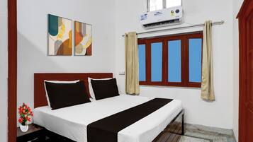 A hotel room with a bed, a window with curtains, an air conditioning unit, and two wall-mounted artworks.