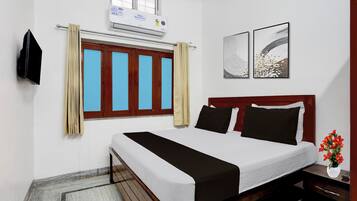 A hotel room with a bed, a nightstand, a vase with flowers, a window with curtains, and two wall art pieces.