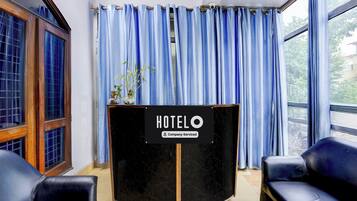 A hotel reception area with a black counter, blue curtains, and two black leather chairs.