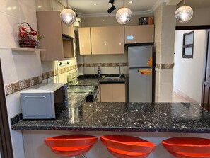 A kitchen with a microwave, refrigerator, and red bowls on the counter. - Modern 2BR Apartment in Rehab (Cairo Governorate)