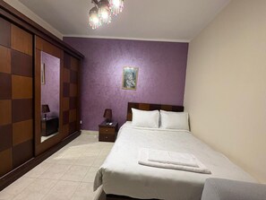 A bedroom with a bed, a nightstand, a mirror, and a chandelier. - Modern 2BR Apartment in Rehab (Cairo Governorate)