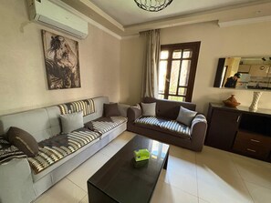 A living room with a sofa set, a coffee table, and a kitchen area visible through an open door. - Modern 2BR Apartment in Rehab (Cairo Governorate)