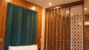 A hotel room with a bed, wooden headboard, ceiling fan, and a decorative partition. - Hotel Oriva (Aligarh)