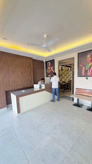 Zona de recepción con mostrador, recepcionista sentada y un huésped de pie.