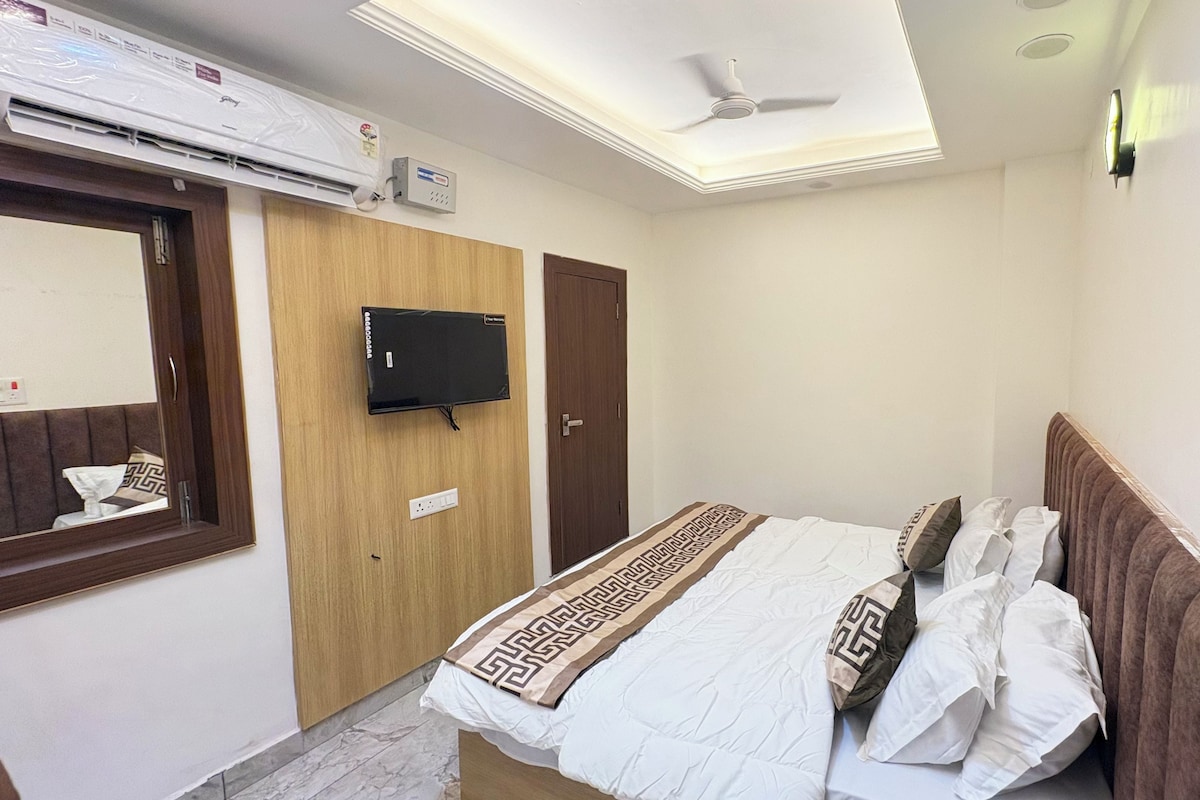 Un dormitorio con una cama, un televisor de pantalla plana en la pared, un ventilador de techo y una ventana.
