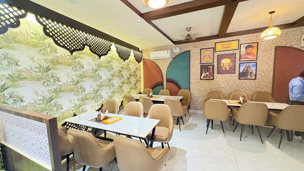A restaurant interior with tables and chairs, decorative wall art, and a patterned wallpaper backdrop.