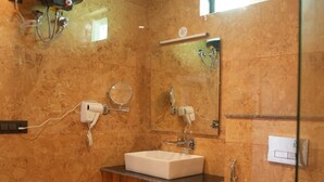 A bathroom with a marble wall, a sink, a mirror, a shower, and a toilet. - Hotel Oriva (Aligarh)