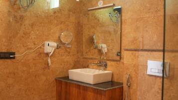 Un baño con pared de mármol, un lavamanos, un espejo, una ducha y un inodoro.