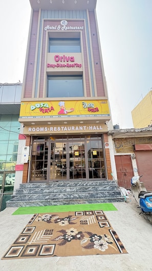 Un hotel con un letrero que dice 'Oriva Stay-Dine-RoofTop' y un colorido cartel para 'DOSA' con diversas opciones de comida.