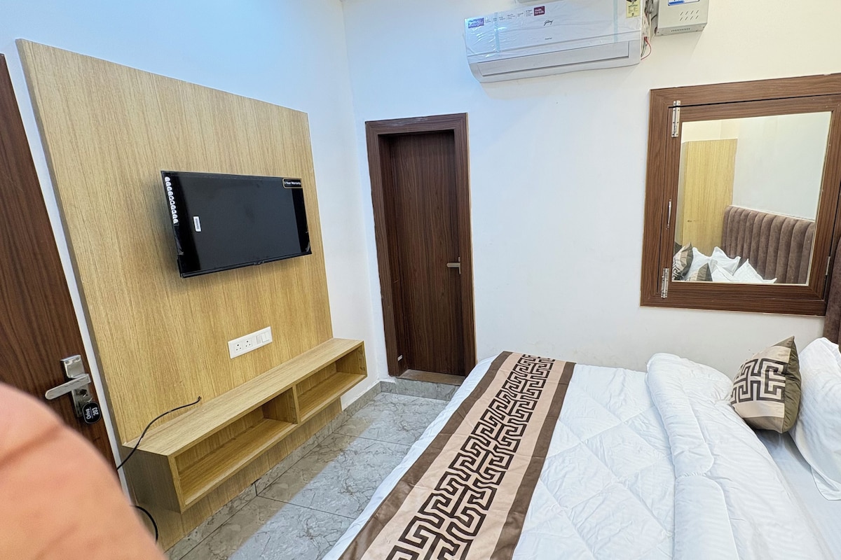 Un dormitorio con una cama, un televisor montado en un panel de madera, una puerta y un espejo con marco de madera.