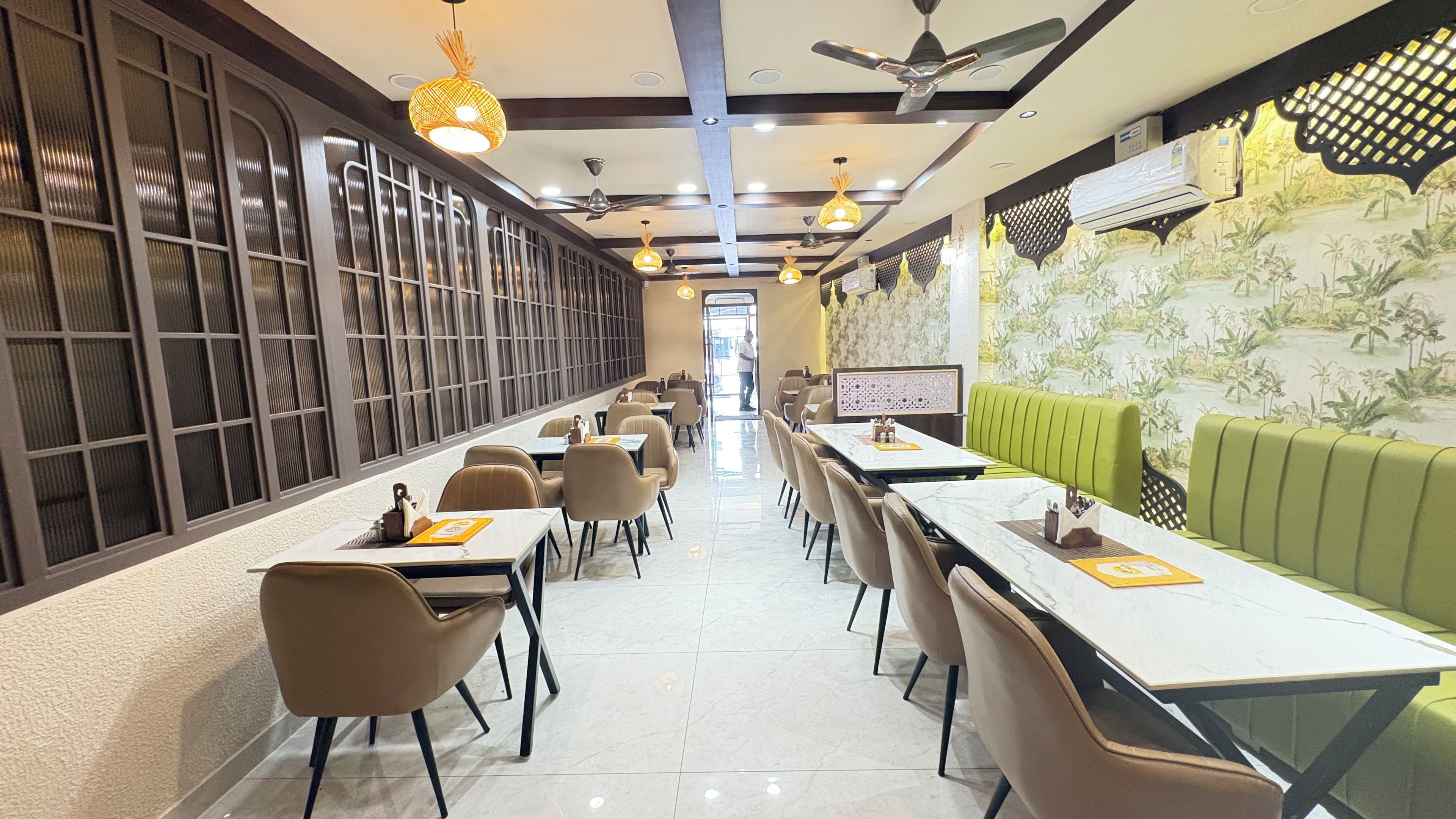 Un restaurante con mesas largas, sillas y una zona con asientos tipo banqueta verde.