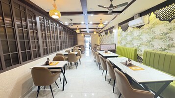 Un restaurante con mesas largas, sillas y una zona con asientos tipo banqueta verde.