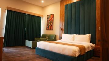 Habitación de hotel con una cama grande, una zona de estar con sillas, un cuadro en la pared y un cabecero de madera.