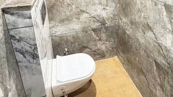 Un baño con inodoro blanco, paredes de mármol y zona de ducha.