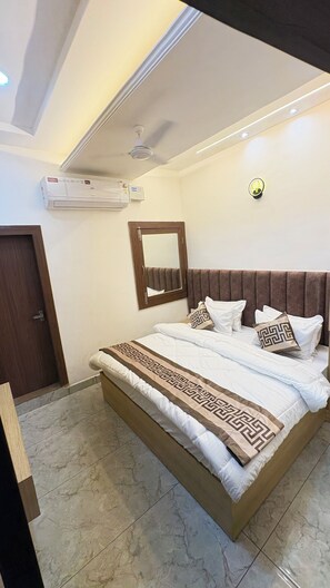 A modern bedroom with a large bed, a ceiling fan, an air conditioning unit, and a mirror on the wall.