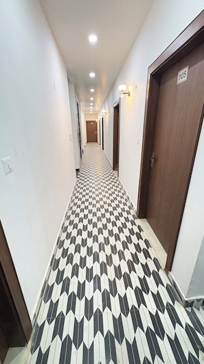 Un pasillo con piso estampado, puertas y luces fijadas a la pared.